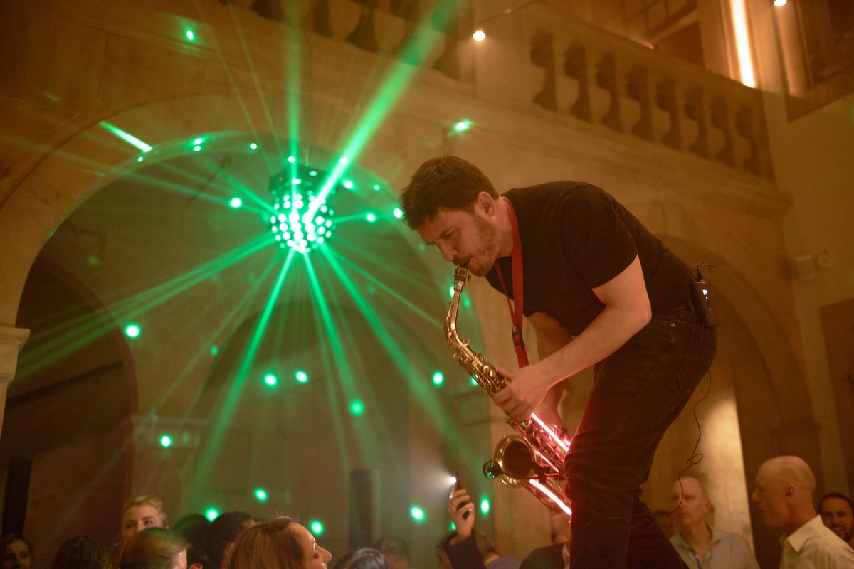 Sax Kid Marbella tocando el saxofón sobre el público, iluminado por luces verdes, durante un evento